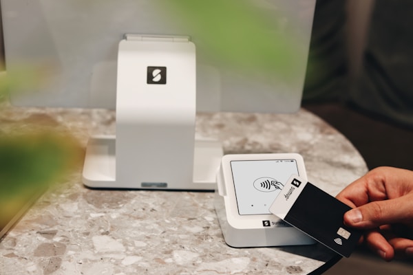 A SumUp Solo card reader is being used to make a contactless payment with a SumUp card. The device is placed on a sleek, modern marble counter, enhancing the overall minimalist and professional aesthetic. The SumUp POS system behind the card reader emphasizes the streamlined and easy-to-use technology, ideal for cafes, boutiques, and other small businesses that value both function and design. This setup reflects a commitment to modern payment solutions with a stylish touch.
